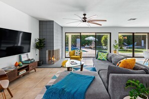 A modern living room with a flat-screen TV, a ceiling fan, a sofa, a coffee table, and a view of a swimming pool.