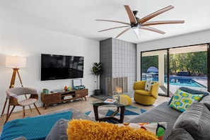 Ein modernes Wohnzimmer mit Flachbildfernseher, Deckenventilator, Kamin und Blick auf einen Swimmingpool.