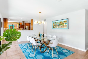 A modern dining area with a glass table, white chairs, and a blue patterned rug.