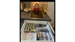 Un tiroir de cuisine contenant des ustensiles, une bouilloire rouge et des pots de confiture.
