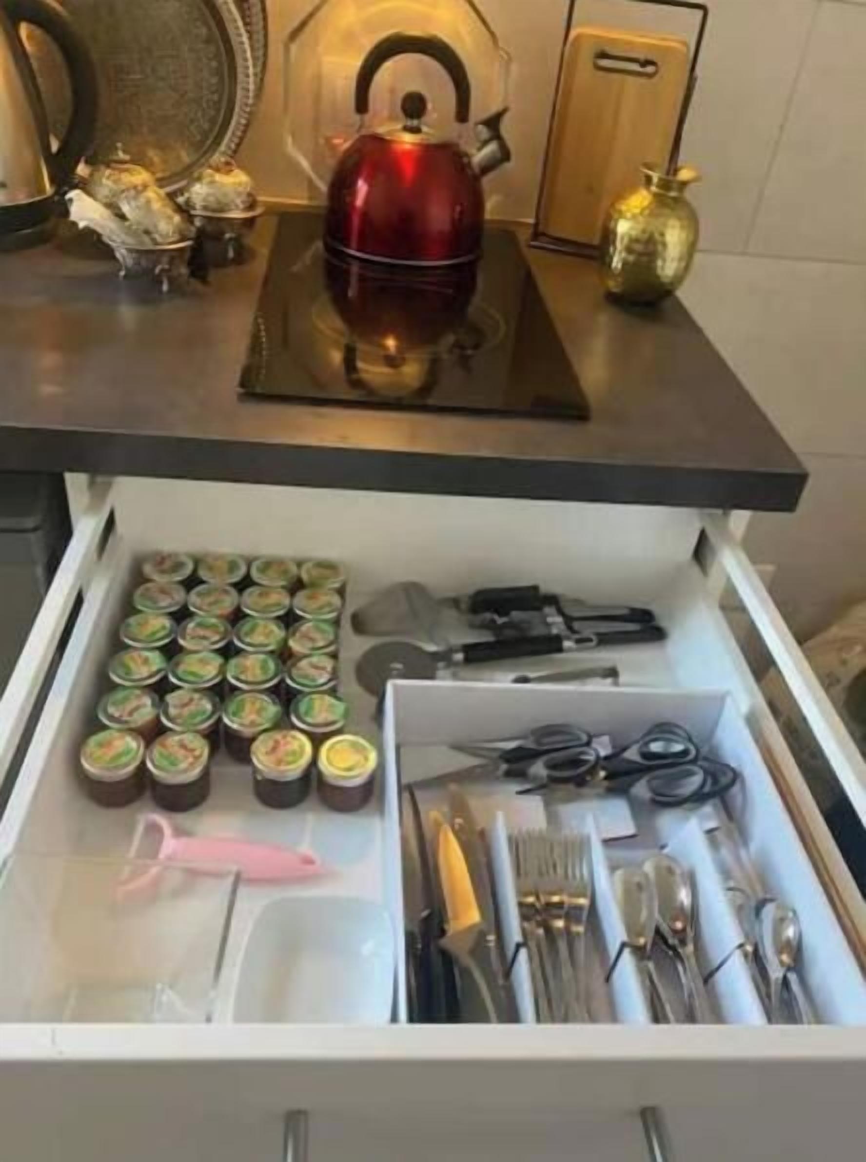 A kitchen drawer with various items including jars, utensils, and a red kettle.