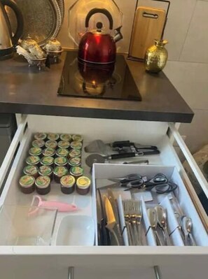 A kitchen drawer with various items including jars, utensils, and a red kettle.