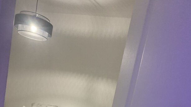 Une chambre à coucher avec un lit, des oreillers, une couverture, un luminaire suspendu et une porte.