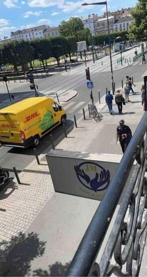 Un fourgon jaune de la société DHL est garé dans une rue de la ville, à proximité d’un passage piéton et d’un panneau représentant un symbole de main.