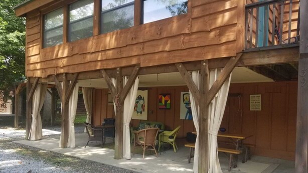 A wooden cabin with a covered patio area featuring outdoor seating and artwork. - The River Joy - Amazing Riverfront Cabin in Franklin NC (Franklin)