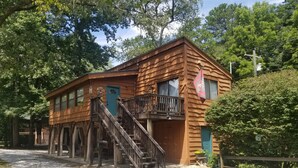 A rustic log cabin with a wooden staircase leading to a balcony, surrounded by trees. - The River Joy - Amazing Riverfront Cabin in Franklin NC (Franklin)