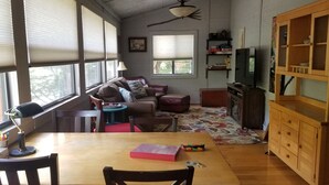 A cozy living room with a wooden table, chairs, a sofa, and a television. - The River Joy - Amazing Riverfront Cabin in Franklin NC (Franklin)