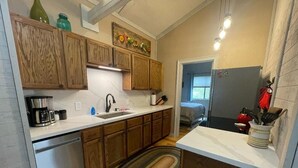A compact kitchen with wooden cabinets, a stainless steel dishwasher, a coffee maker, and a sink. - The River Joy - Amazing Riverfront Cabin in Franklin NC (Franklin)