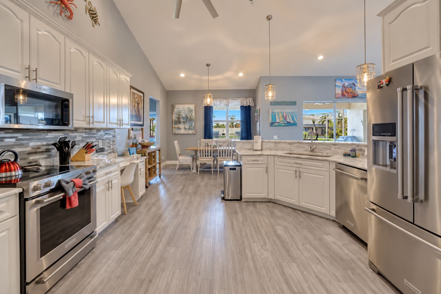 A modern kitchen with stainless steel appliances, a dining area with a view, and a clean, light wood floor.