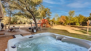 Un jacuzzi en un patio trasero con un área de juegos, un columpio y árboles.
