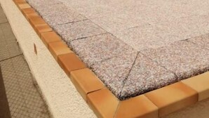 Un edificio de techos planos, amplios ventanales y una zona pavimentada con bordillos.