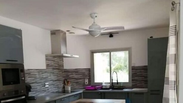 Una cocina compacta con una isla central, taburetes de bar, un microondas y un ventilador de techo.