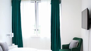 A modern bedroom with a large bed, green curtains, a green armchair, and a flat-screen TV on the wall. - Guthrum Place 3bedroom Luxury Apt Royal Wharf Dock (London)