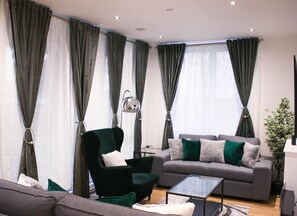 Relax in this stylish living room with a dark green armchair, grey sofa, and glass coffee table.