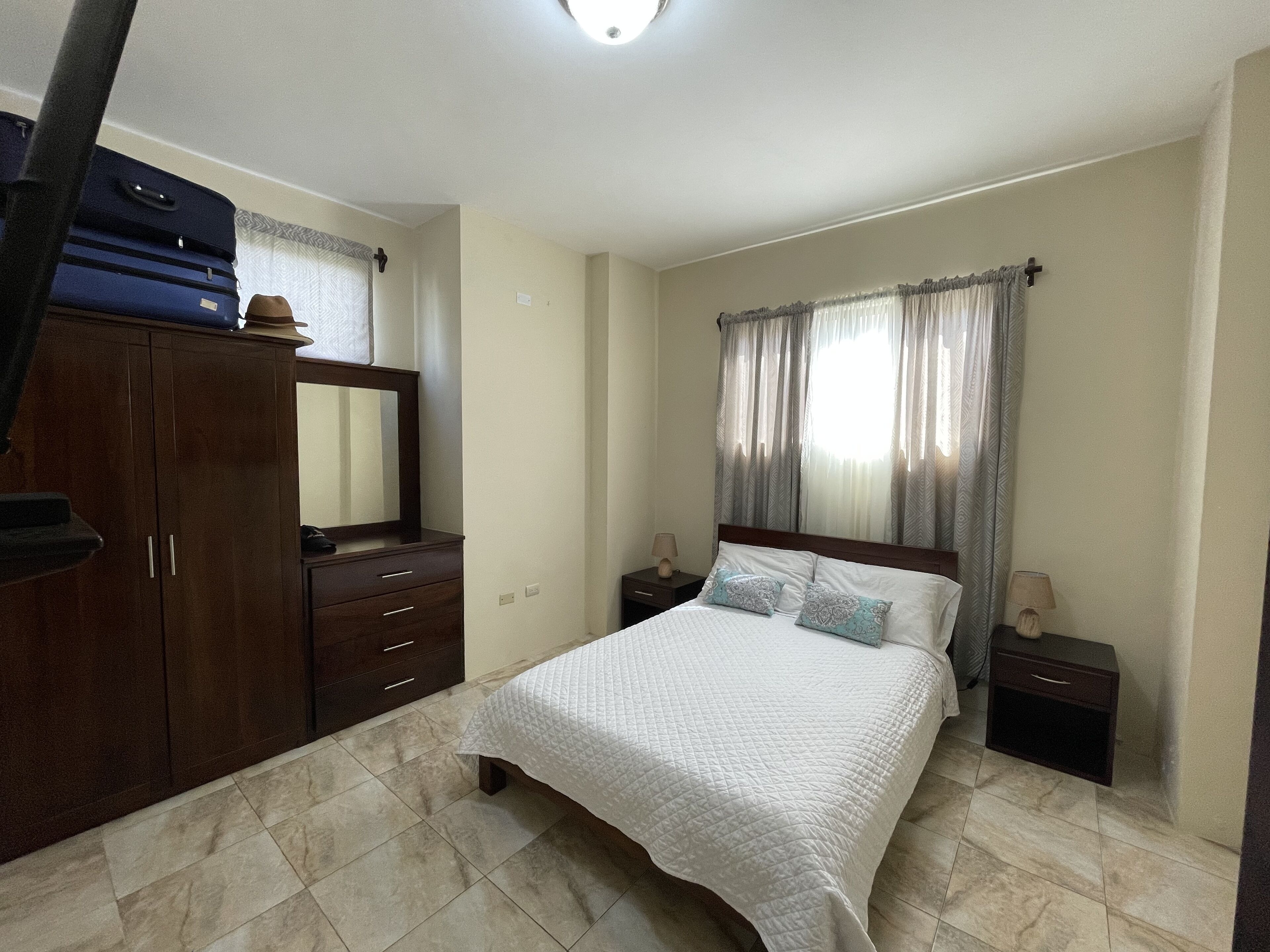 A bedroom with a bed, a wardrobe, a nightstand, a lamp, and a window with curtains.