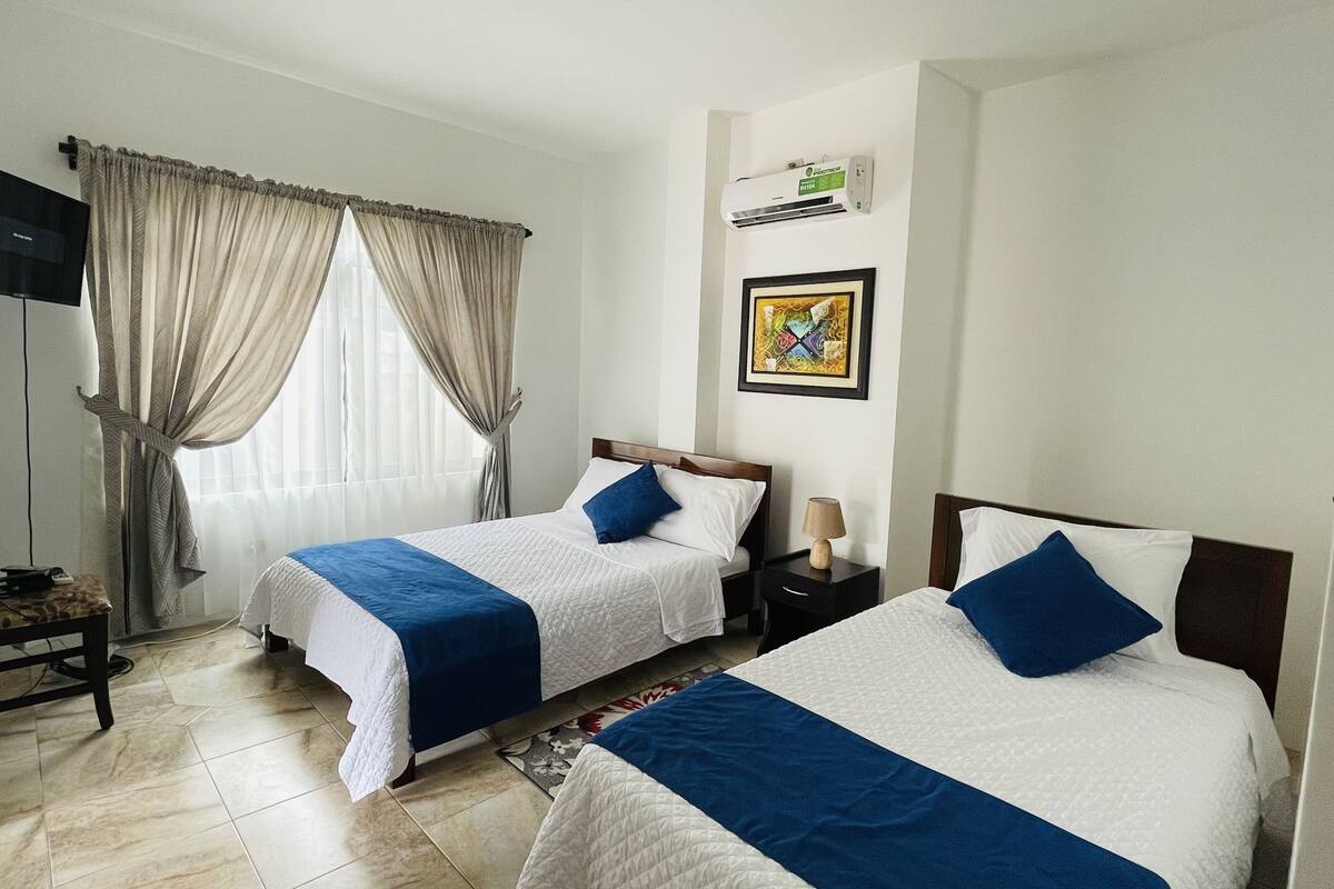 A hotel room with two beds, a flat-screen TV, an air conditioner, and a framed artwork on the wall.
