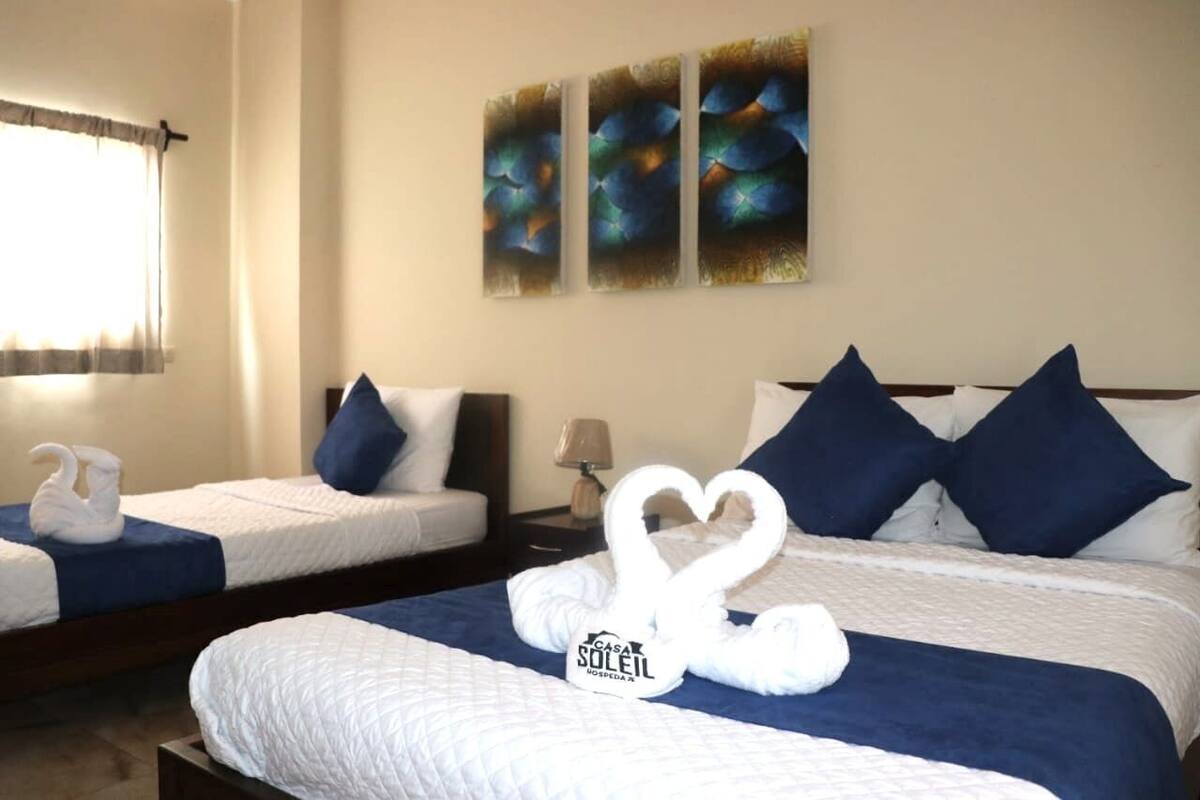 Two hotel beds with white linens, blue pillows, and heart-shaped towels.