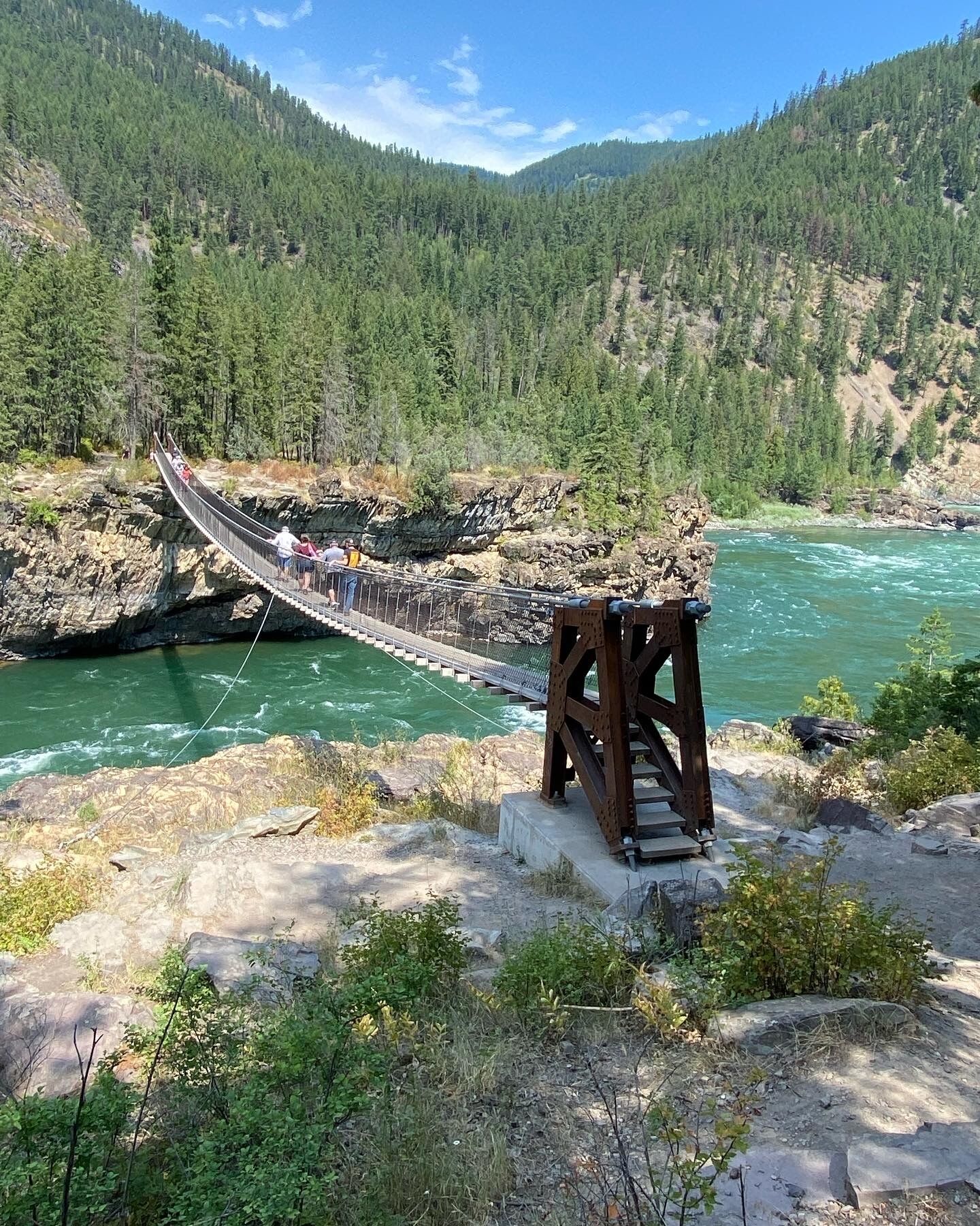 A suspension bridge over a river with a rocky outcrop on the right.