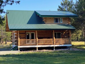 A log cabin with a green metal roof, a front porch with a railing, and a small window. - Authentic Montana wilderness log cabin (pet friendly) (Marion)