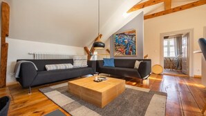 A modern living room with a dark sofa set, a wooden coffee table, and a large painting on the wall.