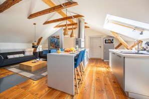 En moderne loftslejlighed med synlige træbjælker, en central ø med barstole, et køkken og en opholdsstue med sofa og sofabord.