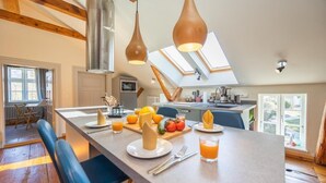 A modern kitchen with a central island, wooden beams, skylights, and a dining area with blue chairs.