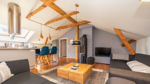 A modern loft apartment with exposed wooden beams, a kitchen area, a dining space, and a living room with a sofa and coffee table.