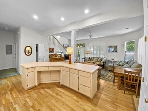 Un vaste espace de vie comprenant une grande cuisine en forme de L, un plancher en bois, un escalier et un coin repas avec une table et des chaises.