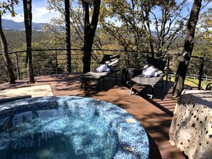 Un jacuzzi rodeado de sillones de descanso y una terraza de madera con vistas a las montañas.