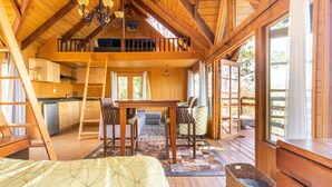 Une cabane chaleureuse avec une chambre à coucher située en mezzanine, un coin repas et une cuisine.