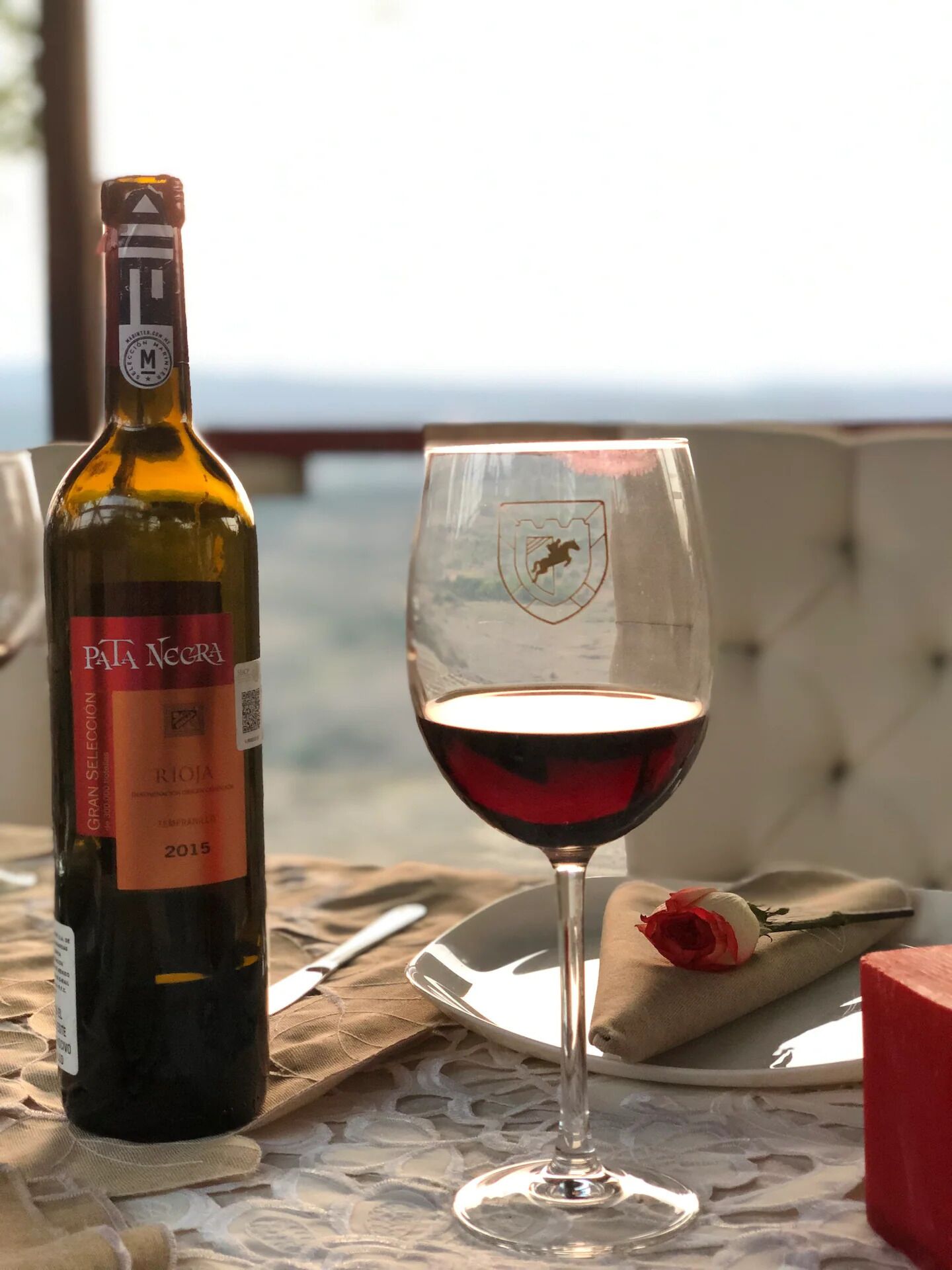 Una botella de vino Pata Negra y una copa de vino tinto sobre una mesa con mantel de encaje.