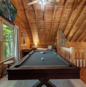 Relax in a cozy space with a pool table, comfortable bed, and natural light.