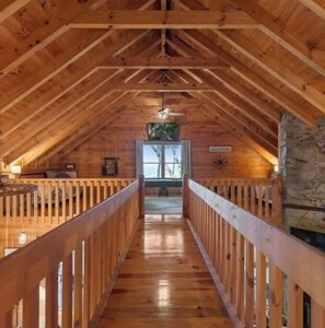 Cozy cabin with a high ceiling, central staircase, and stone fireplace.
