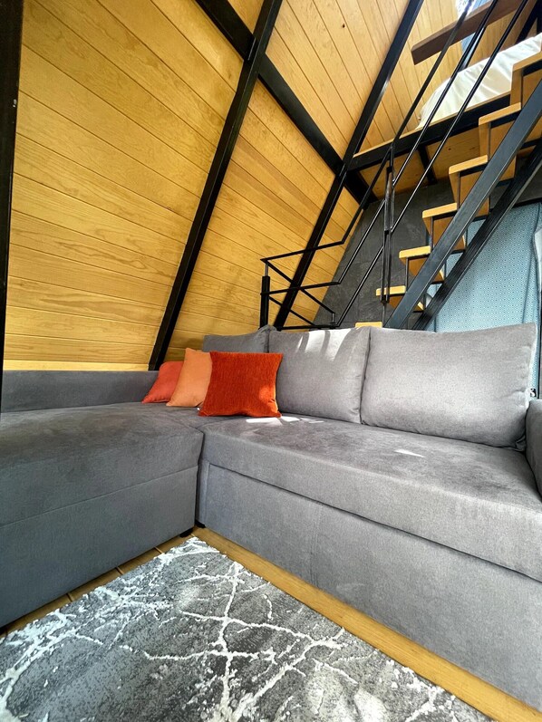 A modern loft bedroom with a grey sectional sofa, a patterned rug, and a wooden ceiling.