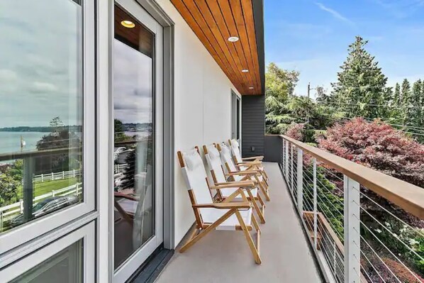 A balcony with a view of a lake, wooden chairs, and a railing.