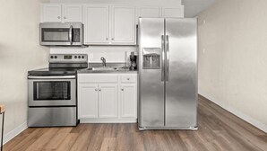 A compact kitchen with white cabinets, a stainless steel refrigerator, a microwave, and an oven.