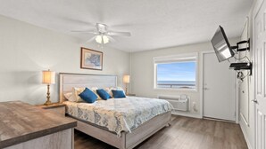 A bedroom with a bed, bedside lamps, a ceiling fan, a TV mounted on the wall, and a window with a view.