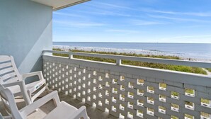 A balcony with white plastic chairs and a white lattice fence overlooking a beach.