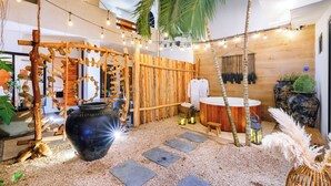 Un área de spa con estructura de madera, una olla negra grande, escalones de piedra, una bañera y luces colgantes.