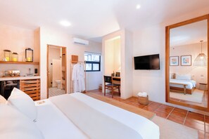Una habitación de hotel moderna con una cama grande, un escritorio, una silla, un televisor y un baño visible a través de una puerta abierta.