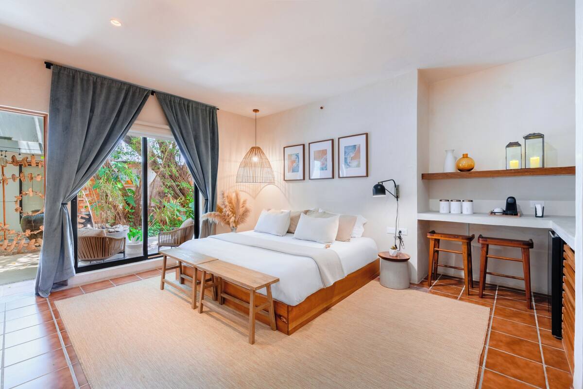 A modern bedroom with a large bed, a desk, and a view of the outdoors.