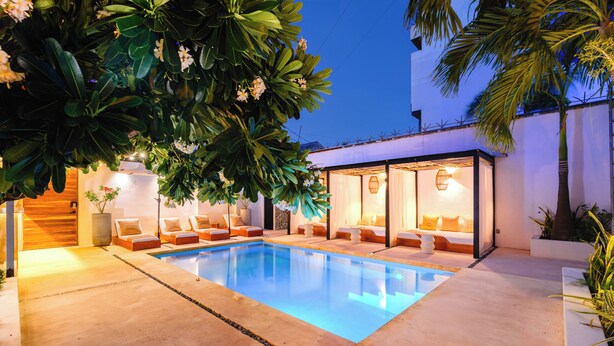 Una piscina con sillas de descanso y una habitación con paredes de vidrio y una cama.