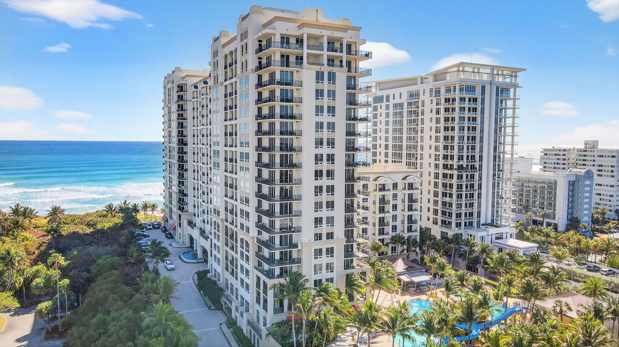 A high-rise hotel with multiple balconies, a swimming pool, and a view of the ocean.