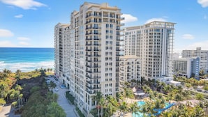 A high-rise hotel with multiple balconies, a swimming pool, and a view of the ocean.
