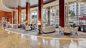 A spacious lobby with marble flooring, large windows, and a seating area with sofas and chairs.