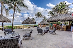 Un espace extérieur aménagé en terrasse, avec des parasols en chaume, des meubles en osier et une vue sur la plage.
