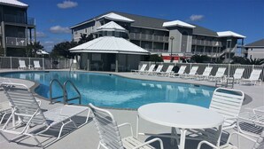 A swimming pool with white lounge chairs and a table, surrounded by a fence. - Balcony to beach in minutes! Orange Beach tranquility all year at great rates! (Orange Beach)