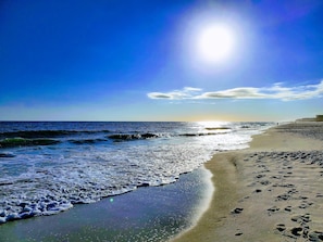 Ein Strand mit Fußabdrücken im Sand, Wellen und einem klaren Himmel.