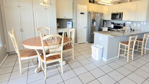 A modern kitchen with white cabinets, a stainless steel refrigerator, a microwave, and a granite countertop island with seating. - Balcony to beach in minutes! Orange Beach tranquility all year at great rates! (Orange Beach)