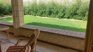 A covered patio area with a stone wall, a grassy lawn, and a view of the garden. - Holiday home for special people (El-Agamy)